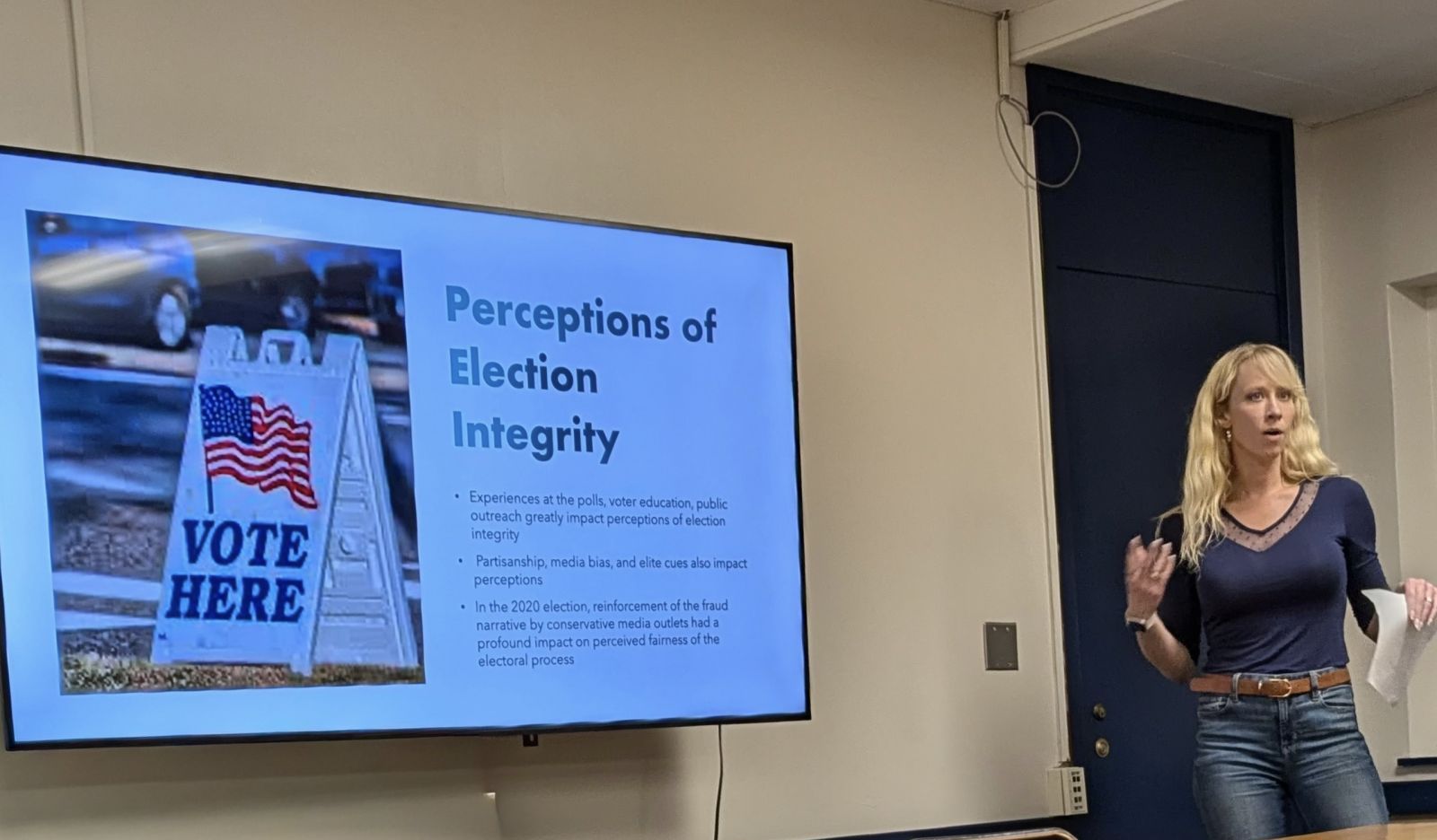 Ashlea Rundlett speaking next to a wall-mounted screen showing a slide titled Perceptions of Election Integrity.